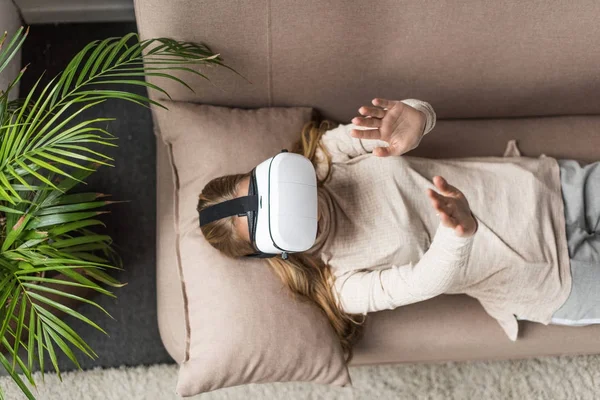 High angle view of young woman in virtual reality headset lying on couch — Stock Photo