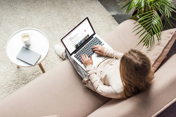 Высокий угол зрения женщины дома сидит на диване и с помощью ноутбука с airbnb сайт на экране — стоковое фото