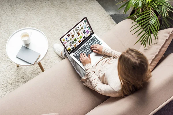 Vista de ángulo alto de la mujer en casa sentado en el sofá y el uso de la computadora portátil con pinterest en la pantalla - foto de stock