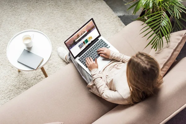 Vista de ángulo alto de la mujer en casa sentado en el sofá y el uso de la computadora portátil con obturador sitio web en la pantalla - foto de stock