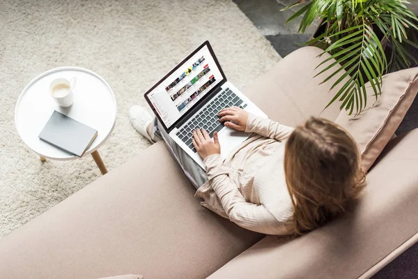Vista de ángulo alto de la mujer en casa sentado en el sofá y el uso de la computadora portátil con el sitio web de youtube en pantalla - foto de stock