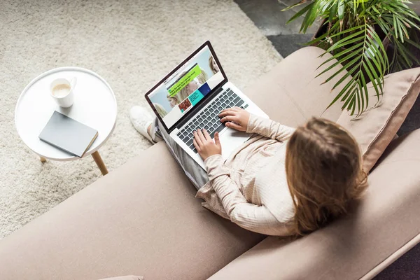 Vista de ángulo alto de la mujer en casa sentado en el sofá y el uso de la computadora portátil con el sitio web de la penes en la pantalla - foto de stock