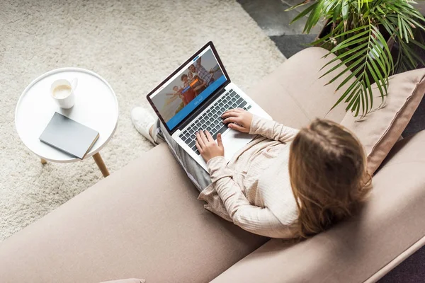 Vista de ángulo alto de la mujer en casa sentado en el sofá y el uso de la computadora portátil con couchsurfing sitio web en la pantalla - foto de stock