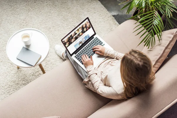 Visão de alto ângulo da mulher em casa sentado no sofá e usando laptop com shutterstock homepage na tela — Fotografia de Stock
