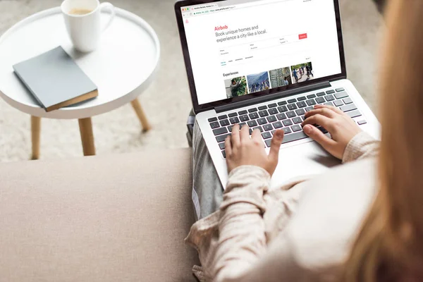 Обрізаний знімок жінка вдома сидячи на дивані і використання ноутбука з веб-сайту airbnb, на екрані — стокове фото