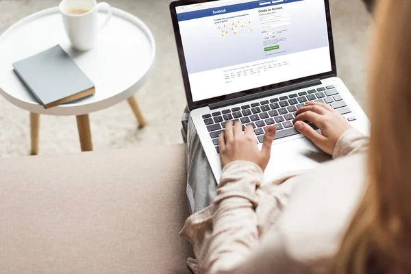 Abgeschnittene Aufnahme einer Frau zu Hause, die auf der Couch sitzt und Laptop mit Facebook auf dem Bildschirm benutzt — Stockfoto