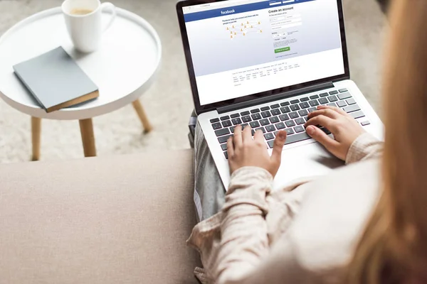 Corte tiro de mulher em casa sentado no sofá e usando laptop com facebook na tela — Fotografia de Stock