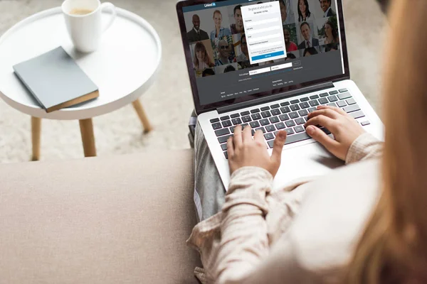 Ritagliato colpo di donna a casa seduta sul divano e utilizzando il computer portatile con linkedin sito web sullo schermo — Foto stock