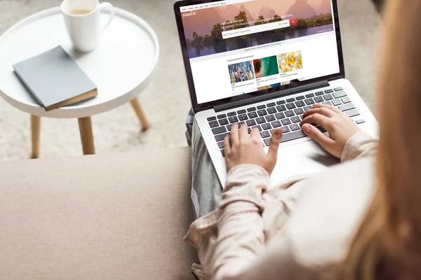 Cropped shot of woman at home sitting on couch and using laptop with shutterstock website on screen — Stock Photo