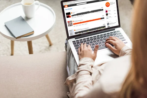 Abgeschnittene Aufnahme einer Frau zu Hause, die auf der Couch sitzt und Laptop mit Soundcloud-Webseite auf dem Bildschirm benutzt — Stockfoto