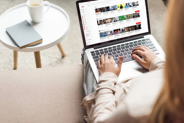 Обрізаний знімок жінка вдома сидячи на дивані і використання ноутбука з сайту youtube на екрані — стокове фото