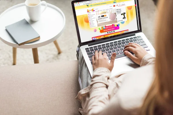 Cropped shot of woman at home sitting on couch and using laptop with aliexpress website on screen — Stock Photo