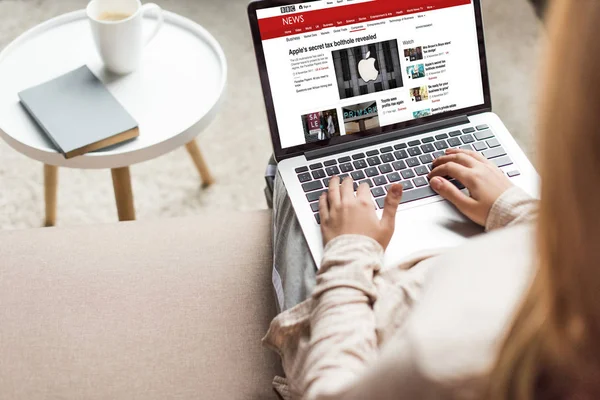 Corte tiro de mulher em casa sentado no sofá e usando laptop com bbc notícias na tela — Fotografia de Stock