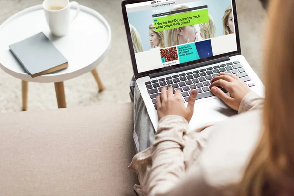Cropped shot of woman at home sitting on couch and using laptop with bbc on screen — Stock Photo