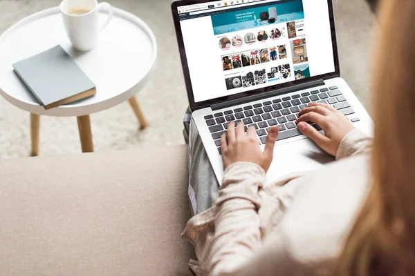 Abgeschnittene Aufnahme einer Frau zu Hause, die auf der Couch sitzt und Laptop mit Amazon-Website auf dem Bildschirm benutzt — Stockfoto