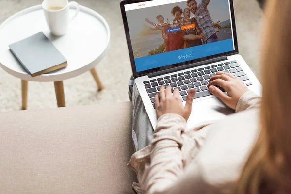 Cropped shot of woman at home sitting on couch and using laptop with couchsurfing website homepage on screen — Stock Photo