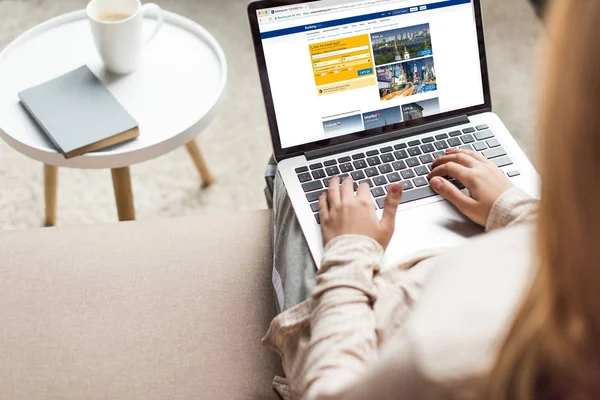 Recortado tiro de la mujer en casa sentado en el sofá y el uso de la computadora portátil con el sitio web de reserva en la pantalla — Stock Photo