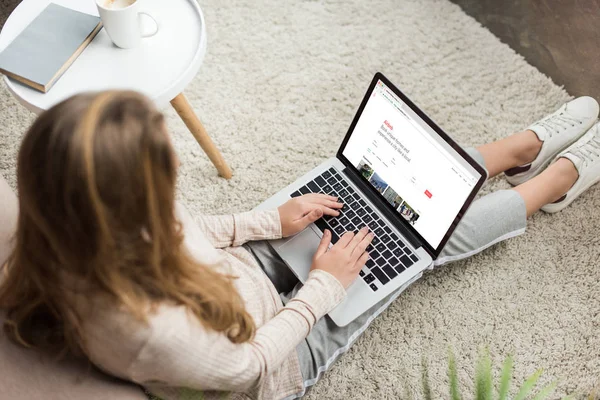 Hochwinkelaufnahme einer Frau zu Hause, die auf dem Boden sitzt und Laptop mit Airbnb-Website auf dem Bildschirm benutzt — Stockfoto