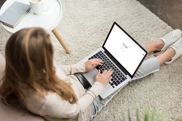 Vista de ángulo alto de la mujer en casa sentado en el suelo y el uso de la computadora portátil con el sitio web de Google en la pantalla - foto de stock