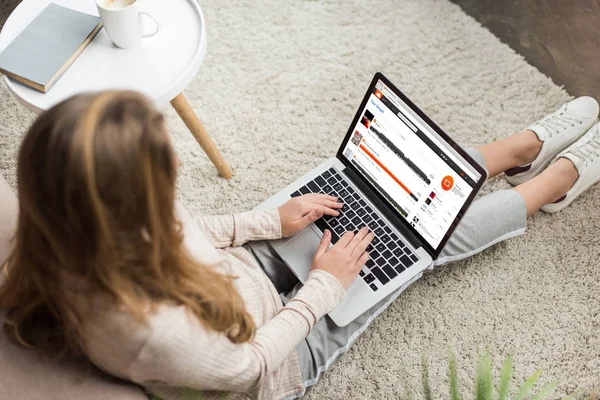 Vista de ángulo alto de la mujer en casa sentado en el suelo y el uso de la computadora portátil con el sitio web soundcloud en la pantalla - foto de stock