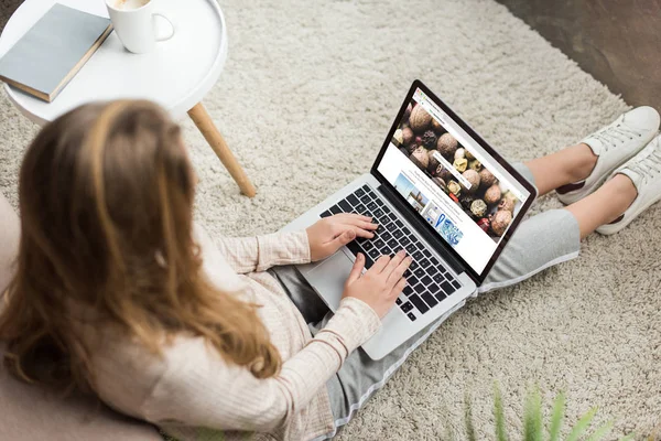 Hochwinkelaufnahme einer Frau zu Hause, die auf dem Boden sitzt und Laptop mit Shutterstock-Webseite auf dem Bildschirm benutzt — Stockfoto