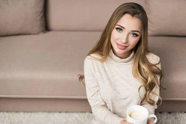 Giovane donna sorridente in maglione caldo con tazza di bevanda calda a casa — Foto stock