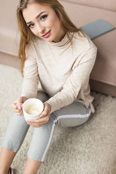 Vue grand angle de belle jeune femme assise sur le sol avec une tasse de café — Photo de stock