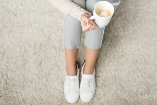 Cropped shot of woman with cup of coffee sitting on floor — Stock Photo