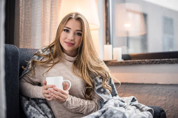 Souriant jeune femme en plaid chaud avec boisson chaude — Photo de stock