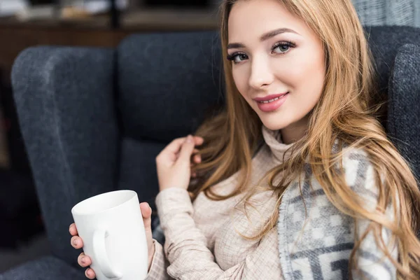 Bela jovem mulher sentada em poltrona confortável com xícara de café — Fotografia de Stock
