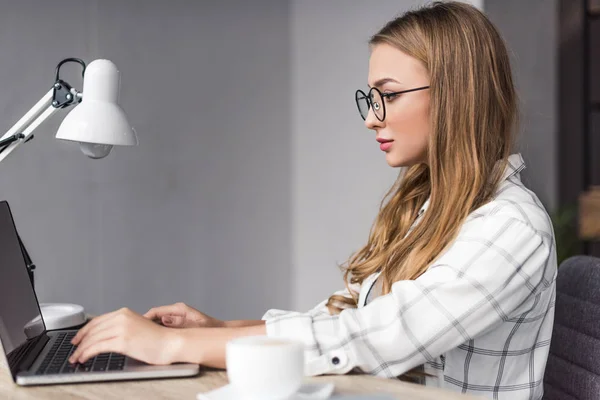 Joven empresaria concentrada que trabaja con el ordenador portátil en el lugar de trabajo - foto de stock