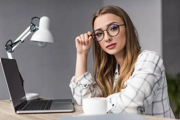 Seria joven empresaria sentada en el lugar de trabajo y mirando a la cámara - foto de stock