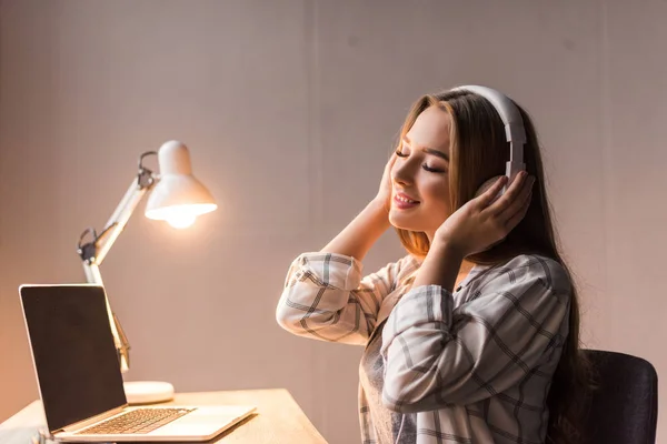 Glückliche junge Frau, die am Arbeitsplatz mit Kopfhörern Musik hört — Stockfoto