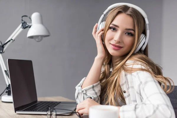 Felice giovane donna ascoltando musica con le cuffie e guardando la fotocamera — Foto stock