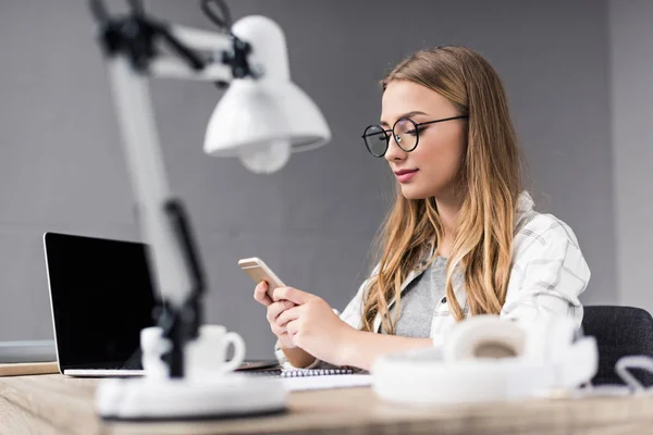 Atractiva joven empresaria usando smartphone en el lugar de trabajo - foto de stock