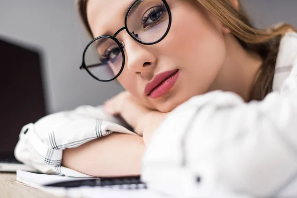 Schöne junge erschöpfte Frau, die auf dem Tisch liegt und in die Kamera schaut — Stockfoto