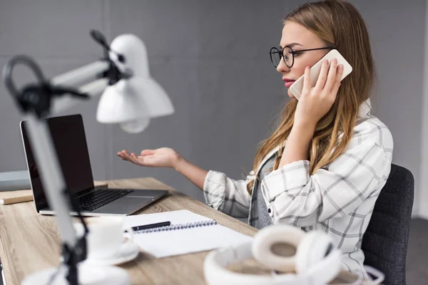 Jeune femme d'affaires surmenée parlant par téléphone sur le lieu de travail et regardant l'écran d'ordinateur portable — Photo de stock