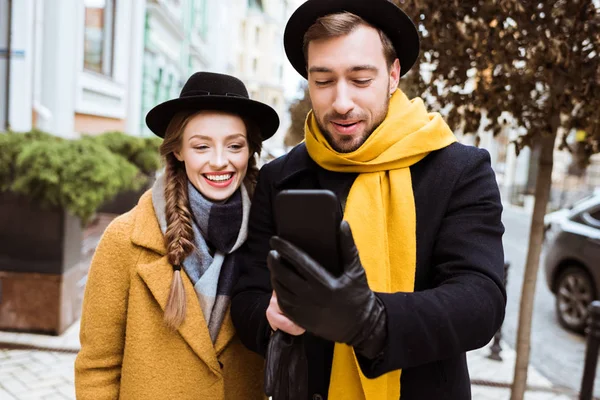 Hermosa pareja joven en traje de otoño mirando el teléfono inteligente - foto de stock