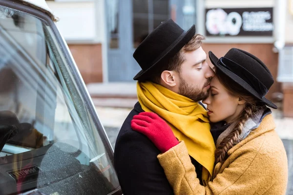 Hermosa pareja joven abrazándose en traje de otoño al lado del coche - foto de stock