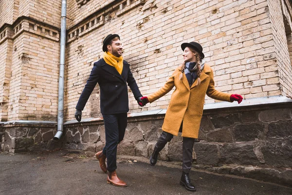 Cute young couple holding hands and running beside old building — Stock Photo