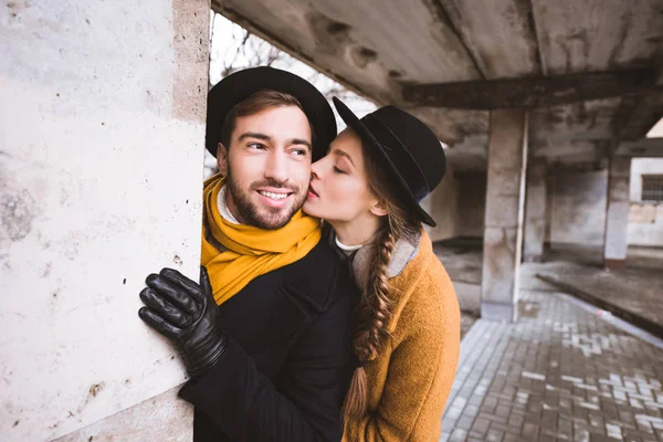 Красивая девушка целует своего бойфренда рядом с колонной — стоковое фото