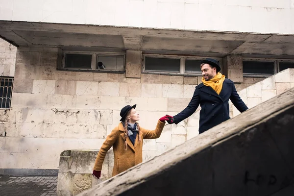 Young couple in autumn outfit holding hands and looking at each other on stairs — Stock Photo