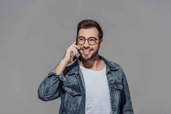 Happy young man talking on smartphone and looking away isolated on grey — Stock Photo
