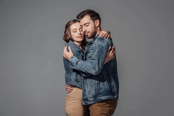 Feliz jovem casal com olhos fechados abraçando isolado em cinza — Fotografia de Stock