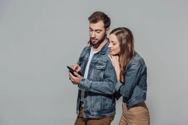 Красива усміхнена молода пара використовує смартфон разом ізольовано на сірому — стокове фото