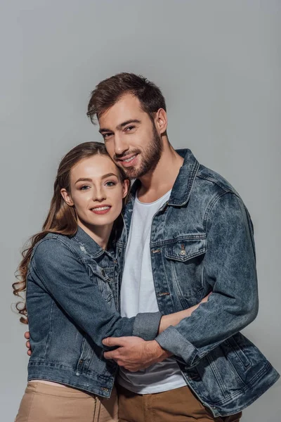 Красива щаслива молода пара обіймає і посміхається на камеру ізольовано на сірому — стокове фото