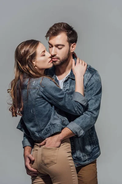 Спокуслива молода пара в джинсових куртках обіймається ізольовано на сірому — стокове фото