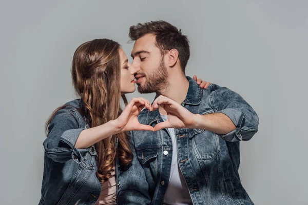 Belo jovem casal apaixonado beijando e mostrando símbolo coração mão isolado no cinza — Fotografia de Stock
