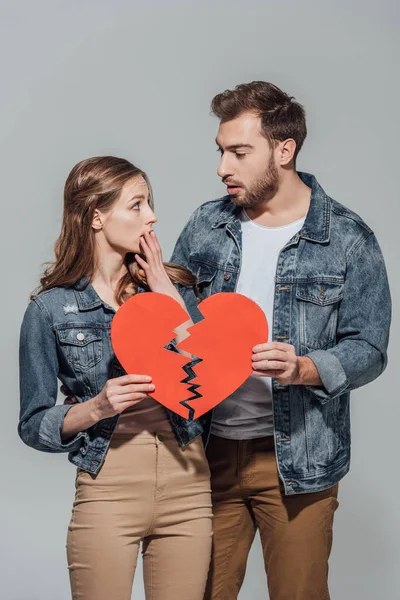 Couple bouleversé tenant des morceaux de symbole de coeur brisé et se regardant isolés sur gris — Photo de stock