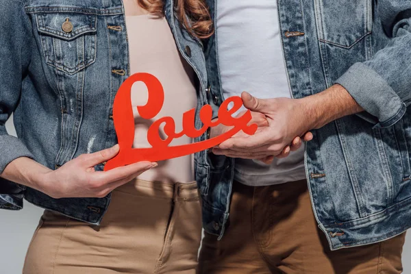 Cropped shot of young couple holding red love symbol isolated on grey — Stock Photo